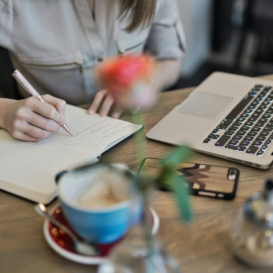 pexels-photo-1766604-1766604 Woman writing in a notebook with a laptop and coffee cup on a desk. Ideal for workspace inspiration.